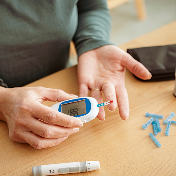Person using a blood glucose meter to check blood sugar with a finger prick test, with lancets and supplies on a table.