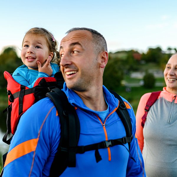 Father hiking with a child in a backpack carrier and a woman nearby, representing active living supported by CRMC diabetes education.
