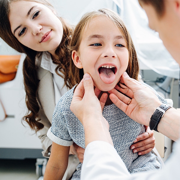 Throat Sick Little Girl In Being Examined By Pediatrician, Sitting On Mom's Lap