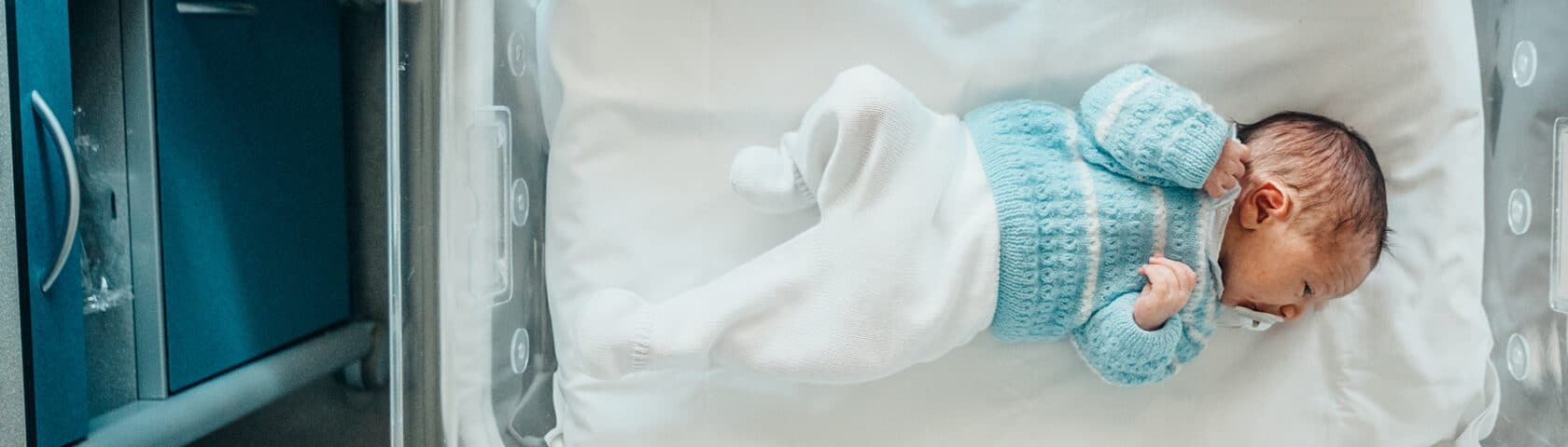 New born baby in a blue sweater and white pants.