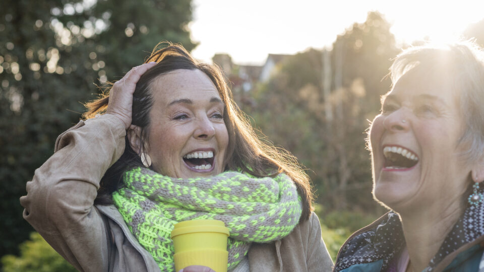 Two women laughing together outdoors on a sunny day, celebrating a joyful, active lifestyle.