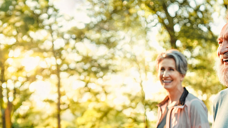 Smiling older couple enjoying a walk outdoors in the sunshine, representing GERD symptom relief and improved quality of life.