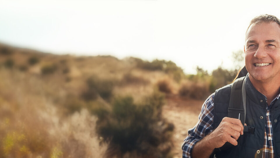 Middle-aged man enjoying a hike outdoors, representing healthy lifestyle habits and awareness for Men’s Health Month in June.