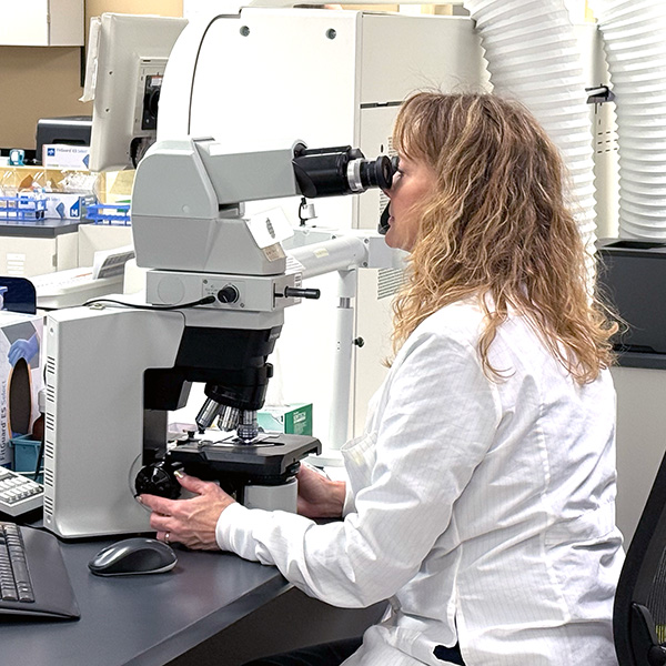 Laboratory professional at Cuyuna Regional Medical Center in Crosby, Minnesota, using a microscope to analyze patient samples in the hospital lab.
