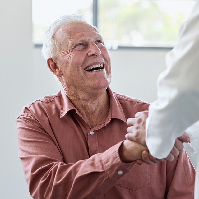 Older adult smiling and shaking hands with a healthcare provider, symbolizing supportive billing assistance at CRMC.
