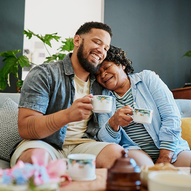 Smiling man and elderly woman enjoying tea together, celebrating comfort and connection made possible through financial relief.