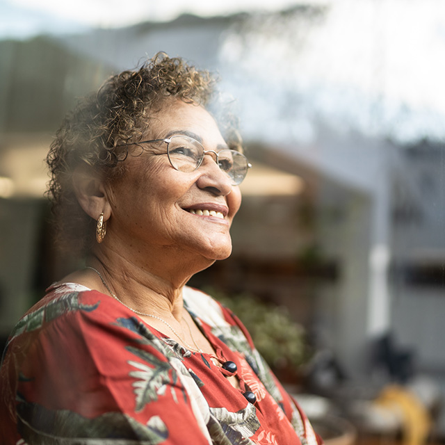 Older woman smiling while looking out a window, representing a sense of peace and financial hope for the future.