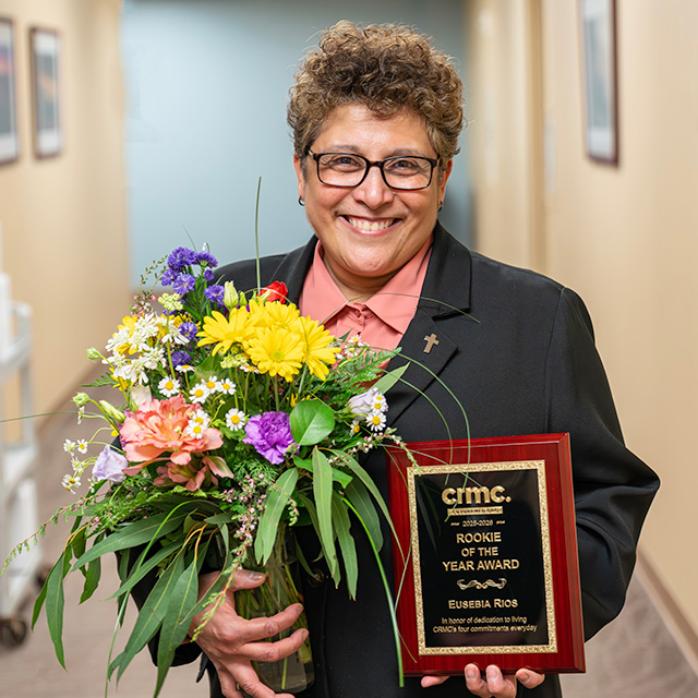 Eusebia Rios smiles while holding the Rookie of the Year award and a bouquet of flowers.
