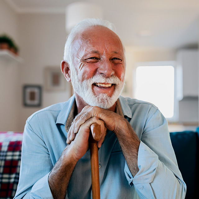 Smiling older man sitting at home with hands resting on a cane, representing reduced financial burden through AblePay.