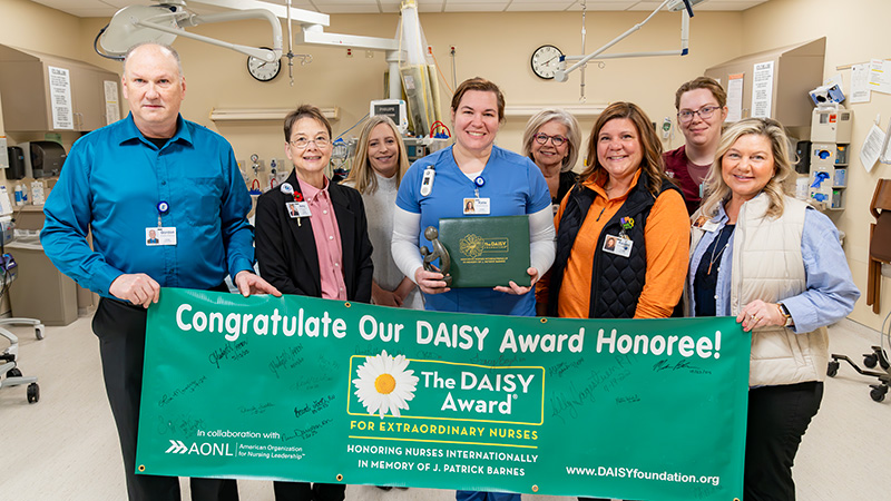 CRMC staff stand with DAISY Award recipient Katie Wieland, RN, who holds her award while the team displays a green banner celebrating her recognition.