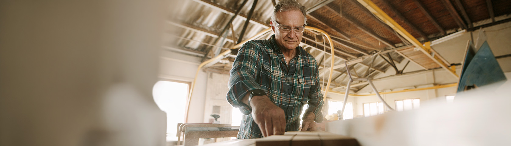 Older man smiling while gardening and holding a potted plant, representing a healthy back, strength, and active lifestyle.