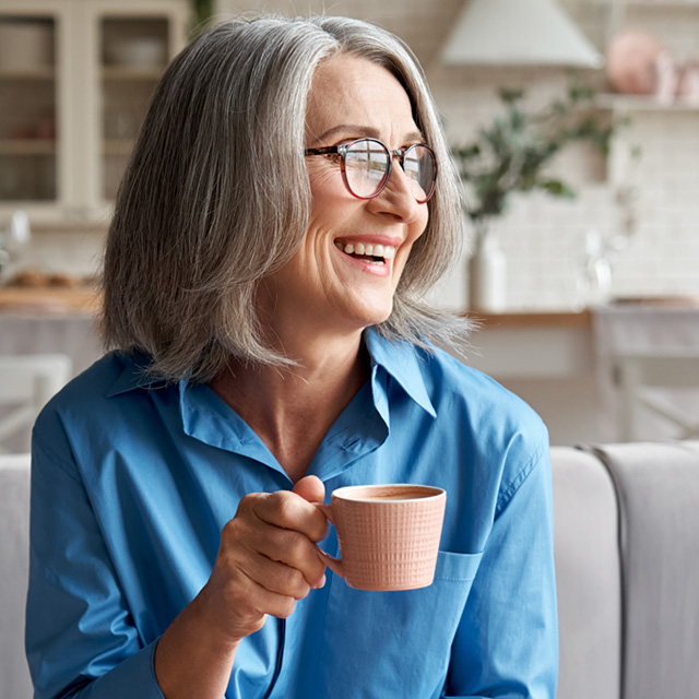 Smiling older woman with gray hair holding a pink mug, preparing for a colonoscopy with a liquid diet.