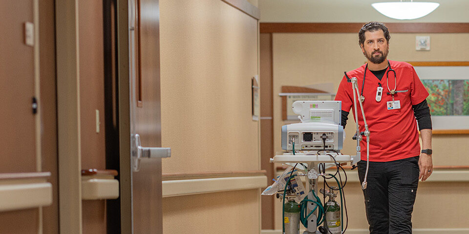 CRMC respiratory therapist in red scrubs transporting respiratory equipment through the hospital hallway.
