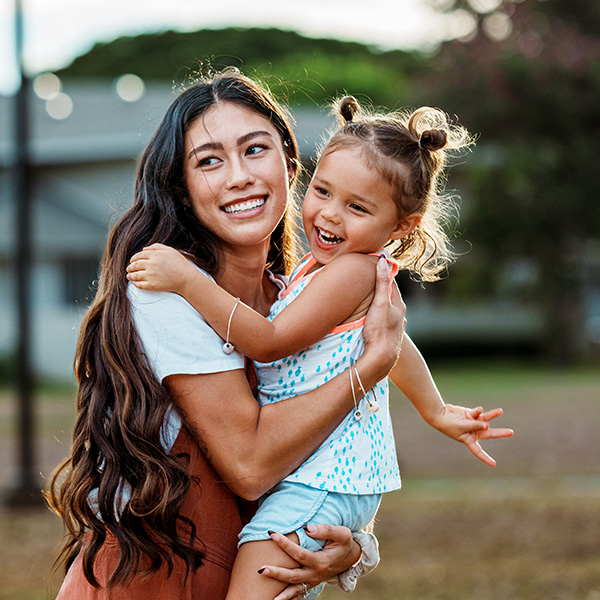A mother holding smiling young child outdoors, illustrating families checking MyChart vaccination records to confirm measles (MMR) immunization status.