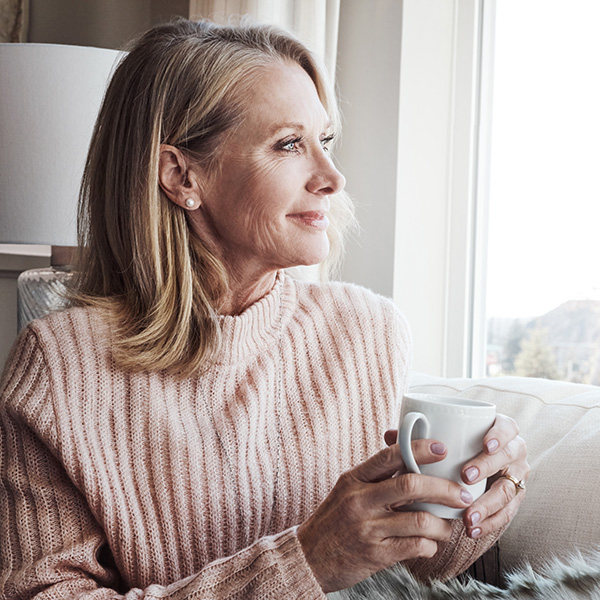 Woman sitting by a window holding a coffee mug, reflecting on future healthcare wishes and advanced care planning.