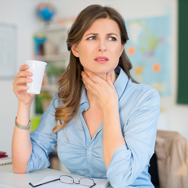 Concerned woman touching her throat while holding a glass of water, showing common GERD and acid reflux symptoms.