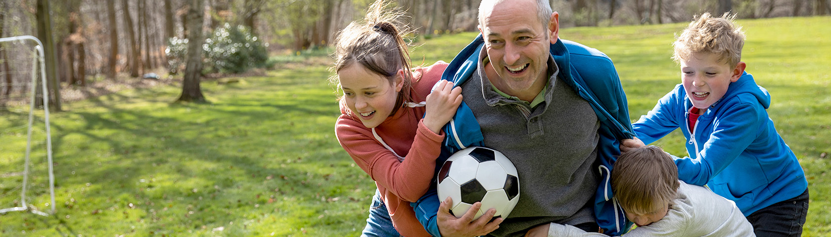 Laughing grandfather playing soccer with grandchildren, representing a healthy spine, flexibility, and joyful, active movement.