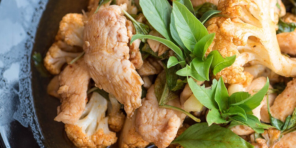 Green Curry Chicken with Cauliflower, garnished with fresh basil, served in a dark bowl as part of a healthy recipe from Cuyuna Regional Medical Center (CRMC)