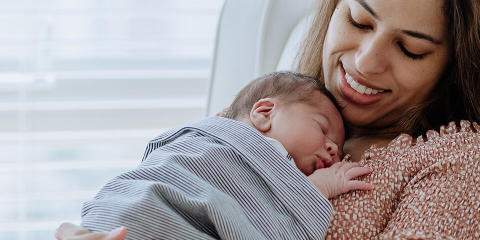 Mother holding healthy newborn wrapped in striped blanket, smiling warmly after delivery at Cuyuna Regional Medical Center (CRMC).