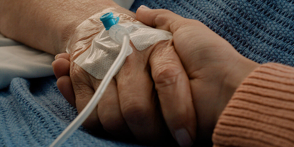 Close-up of a patient’s hand with an IV line being held by a caregiver, symbolizing support during CRMC’s IV fluid supply crisis response.