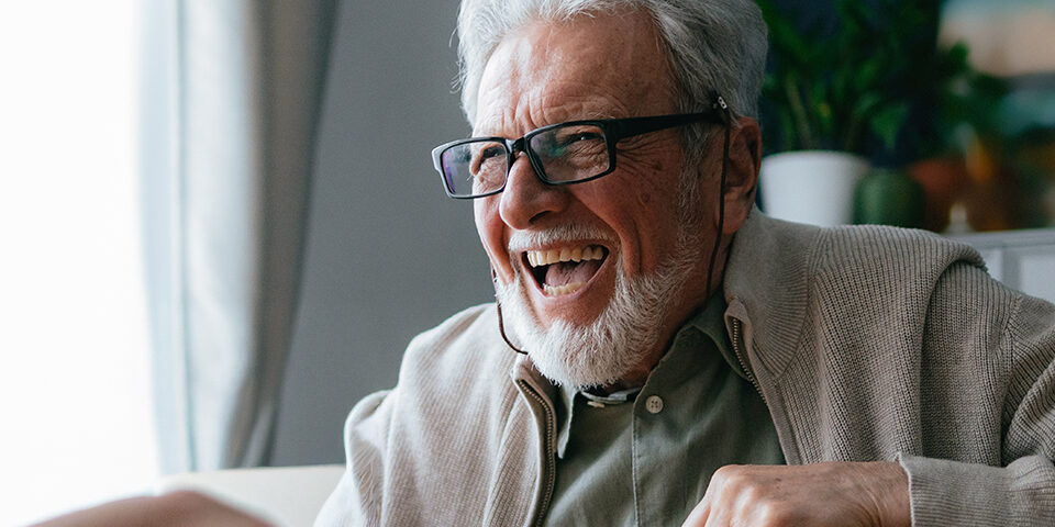Smiling older man with glasses laughs during a visit at home, illustrating CRMC’s new Neurology services bringing expert care close to home in Crosby, MN.