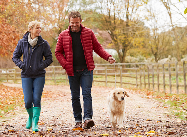Smiling couple walking outdoors with their dog, symbolizing active living made possible with incontinence treatment from CRMC urology.