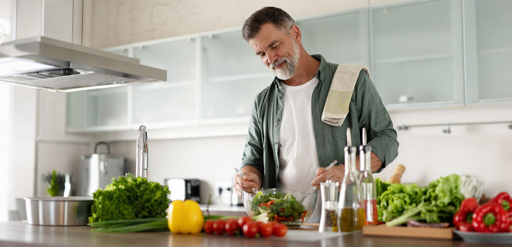 Man preparing a healthy salad with fresh vegetables in a bright kitchen, representing nutrition and the importance of protein during National Nutrition Month.