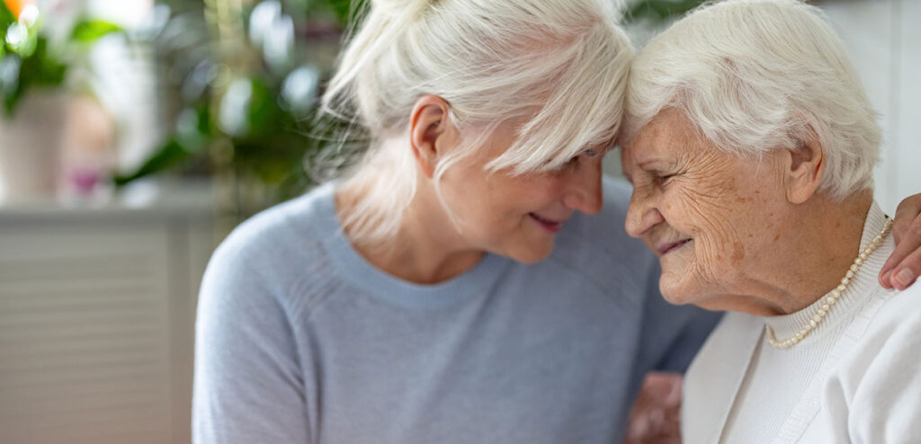 Caregiver comforting an older woman at home, representing support, compassion, and partnership in caring for a loved one with dementia.