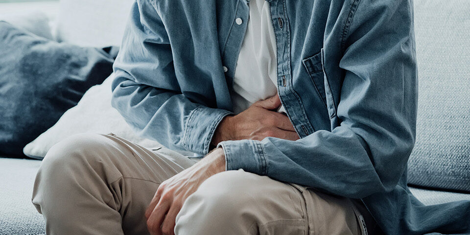 Person sitting on a couch holding their stomach due to abdominal pain and discomfort with gastroparesis.
