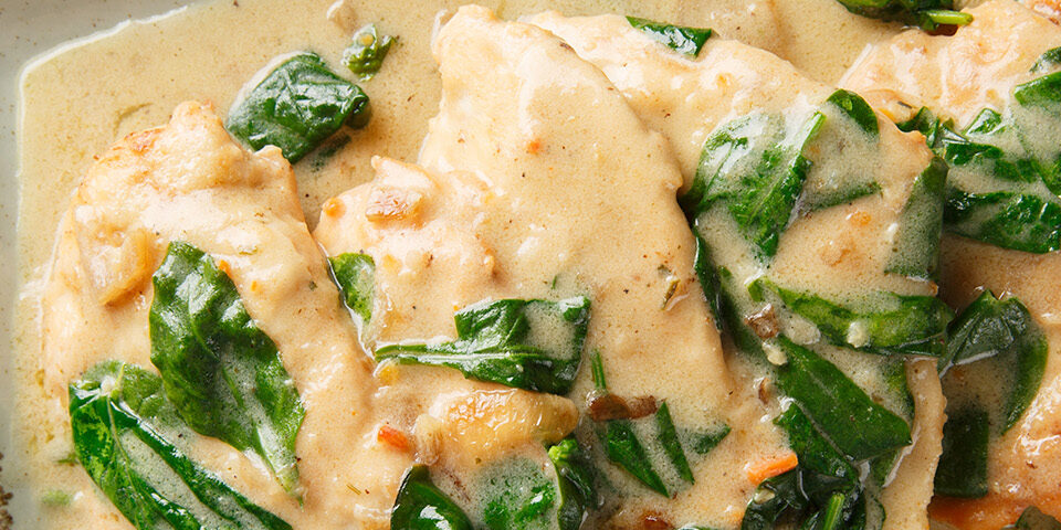 Maple Mustard Chicken topped with fresh spinach and served in a creamy maple mustard sauce on a rectangular plate.